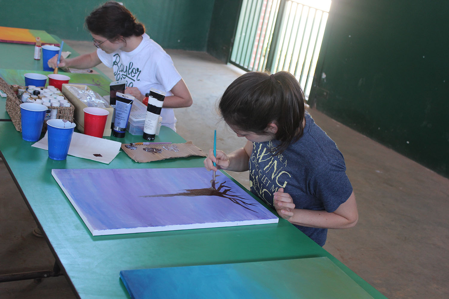 Baylor students Veronica Campbell (front) and Rachel Taylor (back) painted abstract backgrounds and trees on canvases to raise funds for the Family Legacy Tree of Life Children's Village in Zambia. (Photo/Baylor University) 