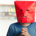 Portrait of shy guy in red paper bag over head