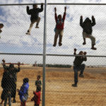 Syrian refugee children climb on a fence to watch a football training workshop in a refugee camp to provide Syrian and Jordanian trainers with football training skills, at Azraq refugee camp near Al Azraq city, Jordan